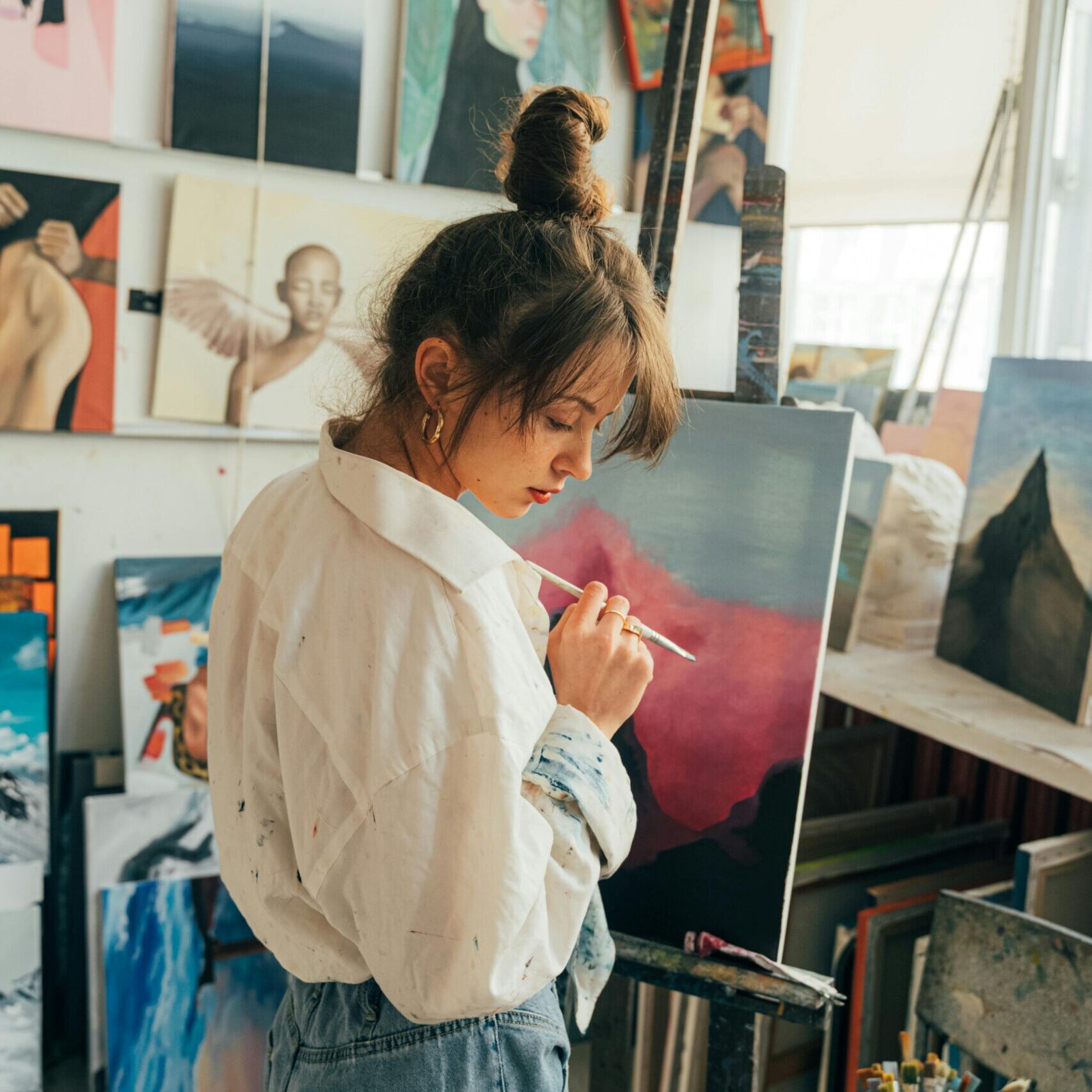 Creative young female artist working in a vibrant art studio filled with paintings